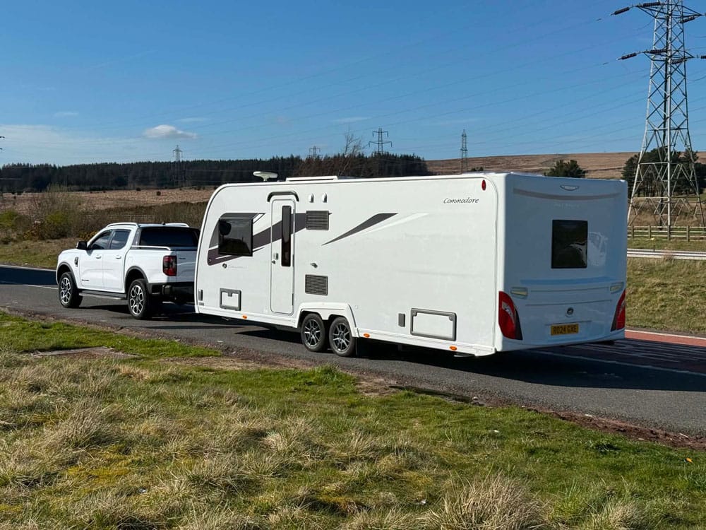 Commodore twin-axle touring caravan towed by a Ford Ranger pickup on a moorland road